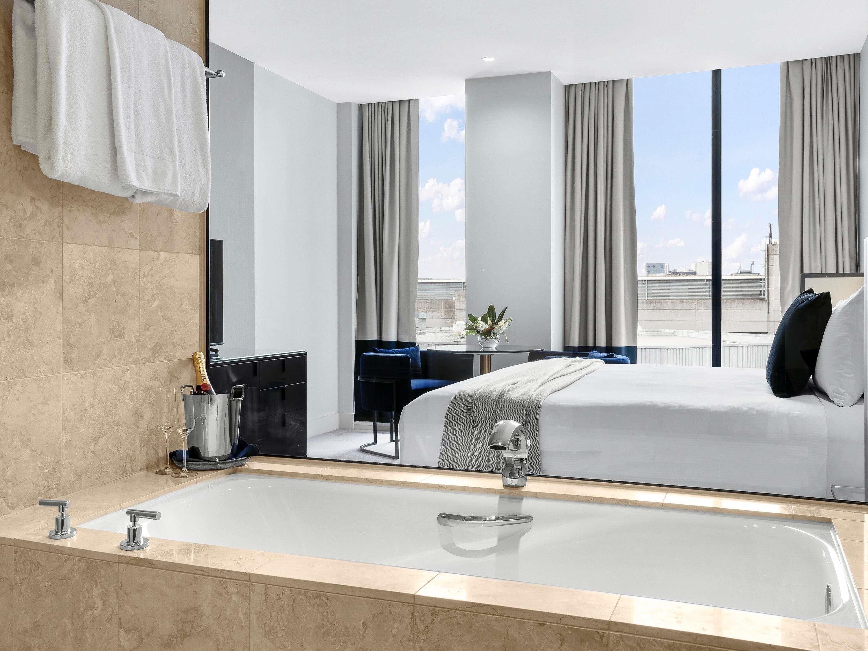 Una habitación de hotel moderna con una bañera grande, una cama, un escritorio y vistas a la ciudad.