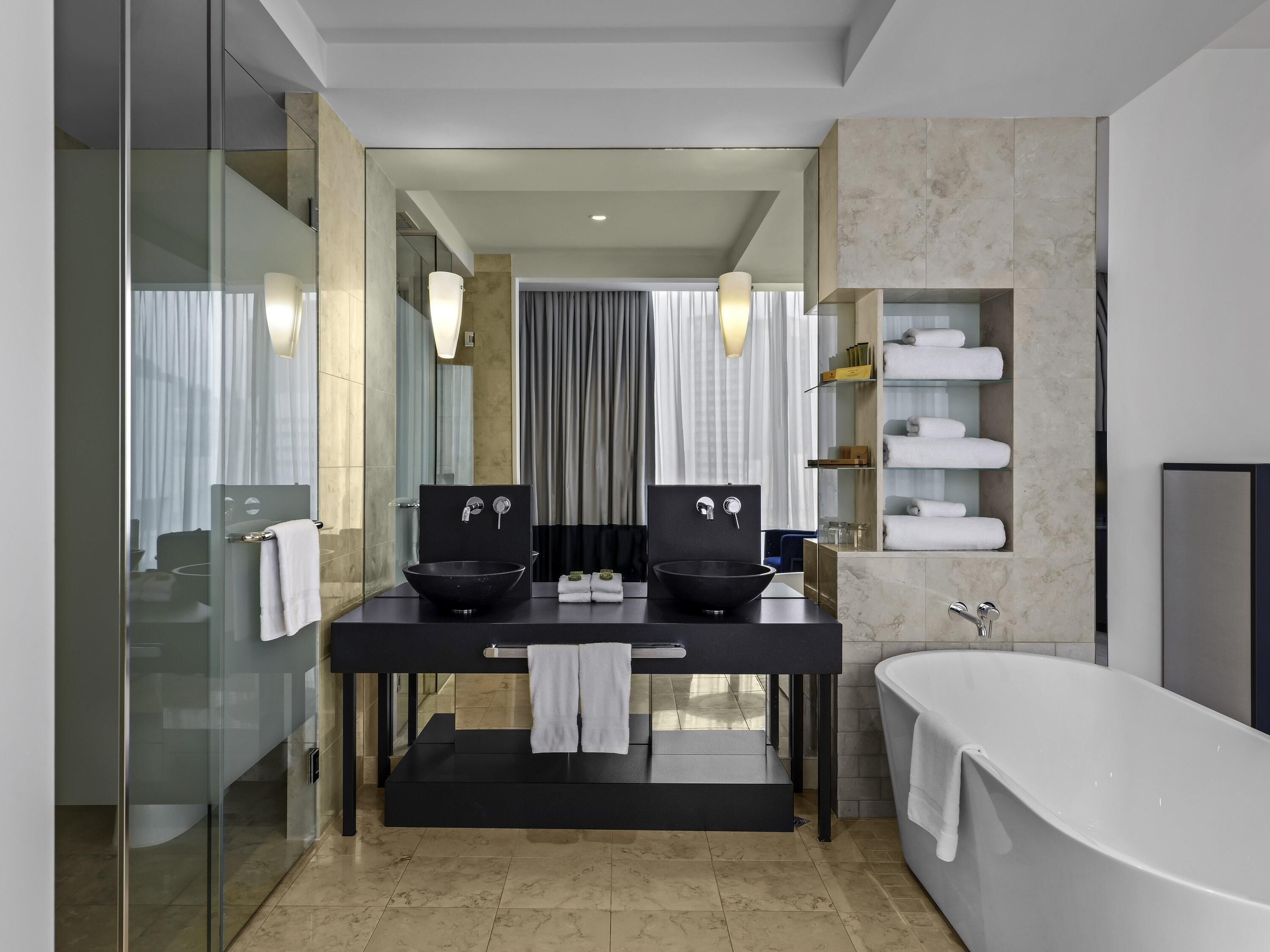 A modern bathroom with a black vanity, two sinks, a bathtub, and a glass shower enclosure.