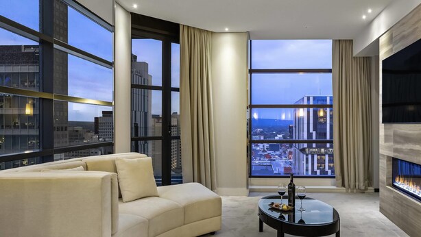 A modern living room with a large window, a sofa, a coffee table with glasses and a bottle, and a fireplace. - Peppers Waymouth Adelaide (Adelaide)