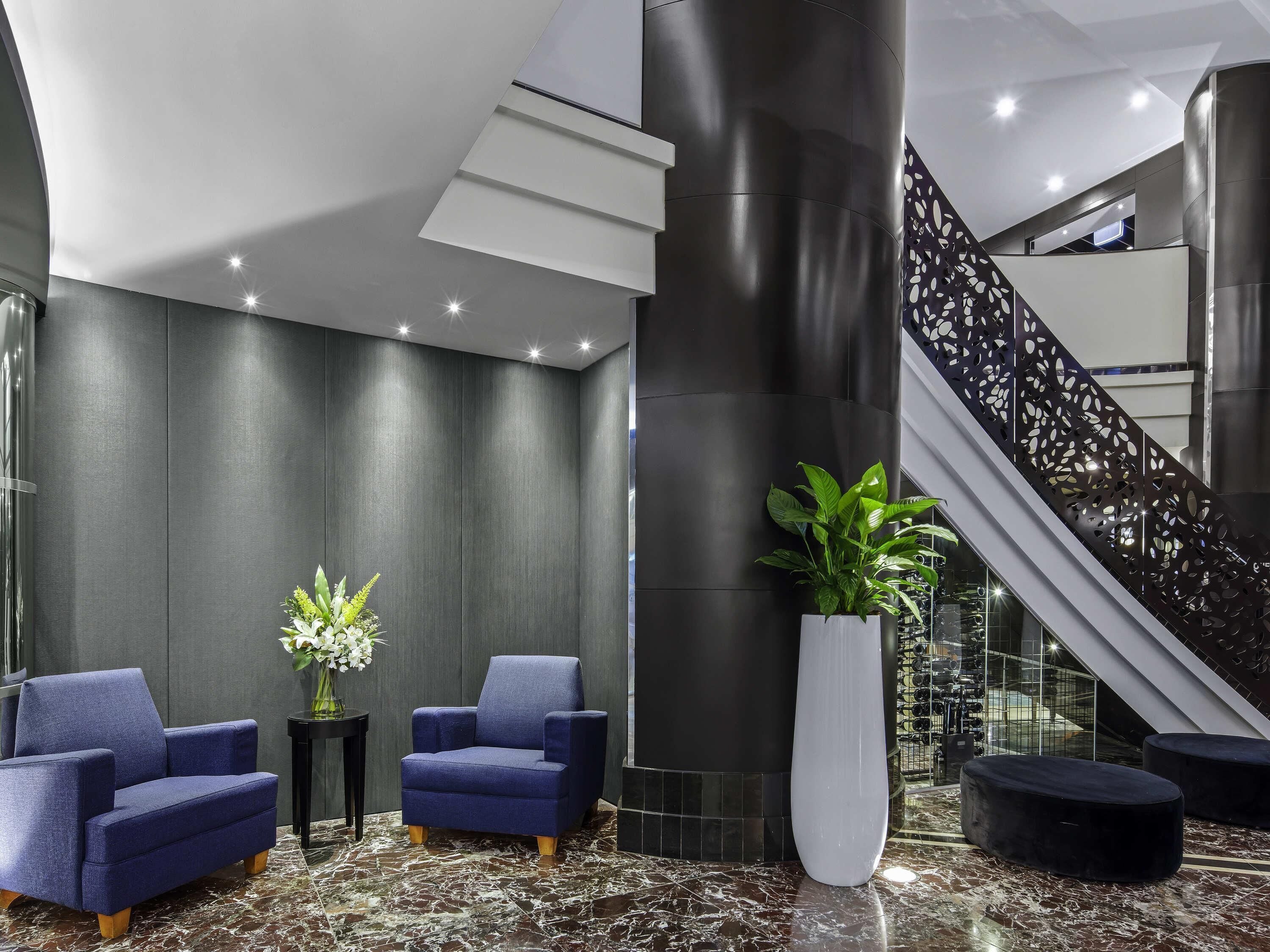 Un vestíbulo moderno con paredes oscuras, piso de mármol y una escalera con barandilla decorativa.