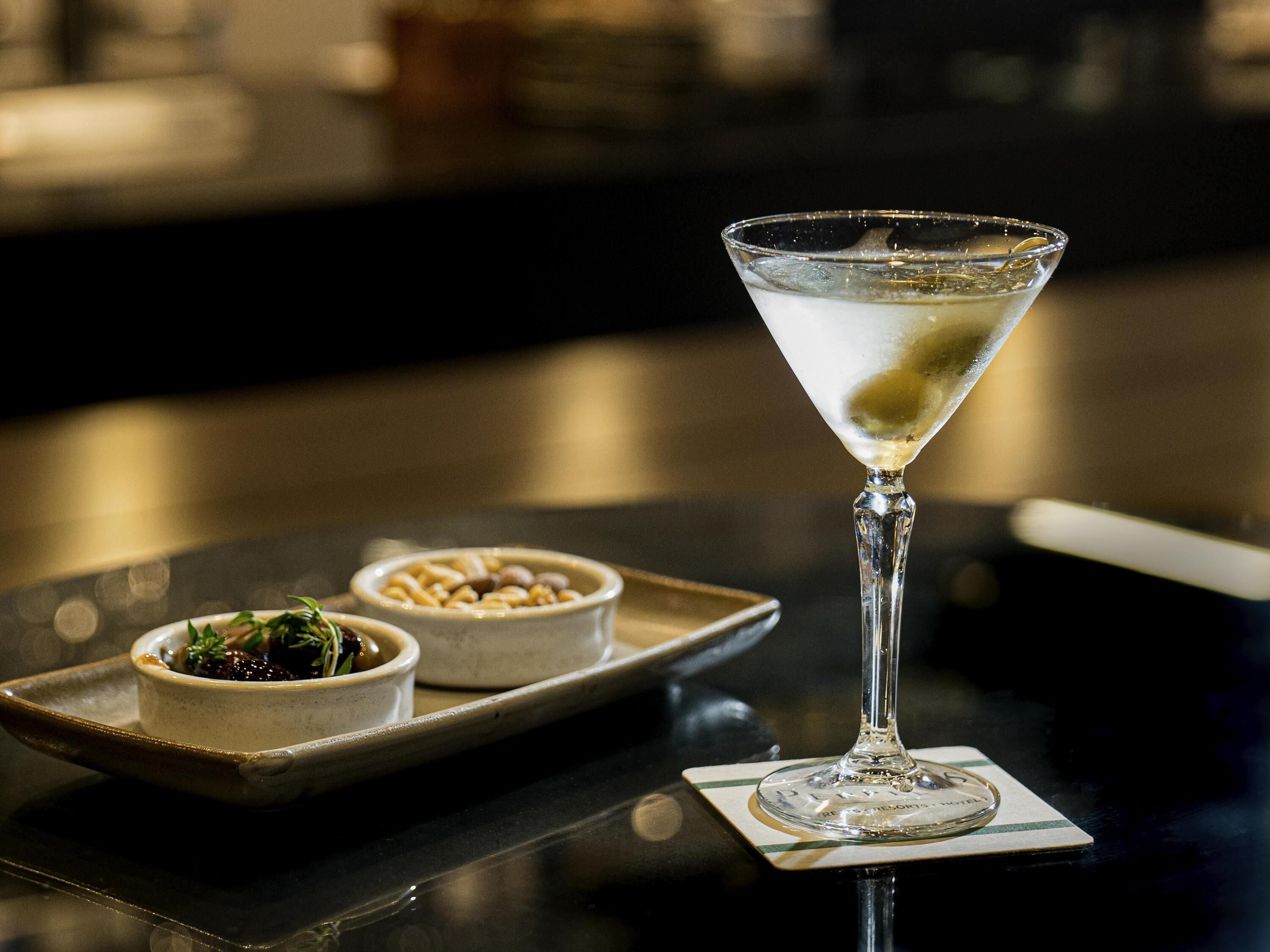 Um copo de martini sobre um apoio com uma bandeja contendo duas pequenas tigelas de comida.