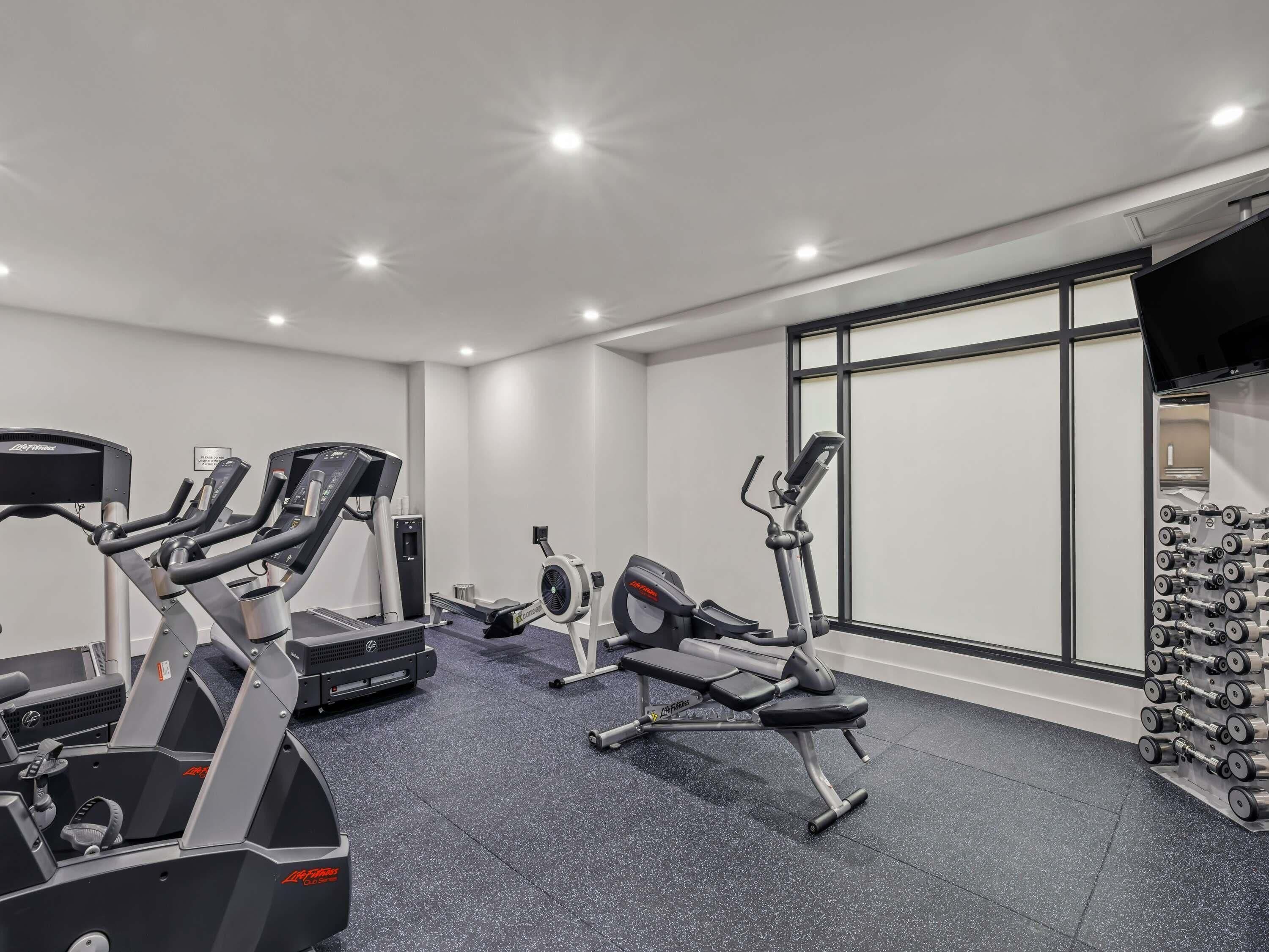 A gym with treadmills, an elliptical, a stationary bike, and a rack of dumbbells.