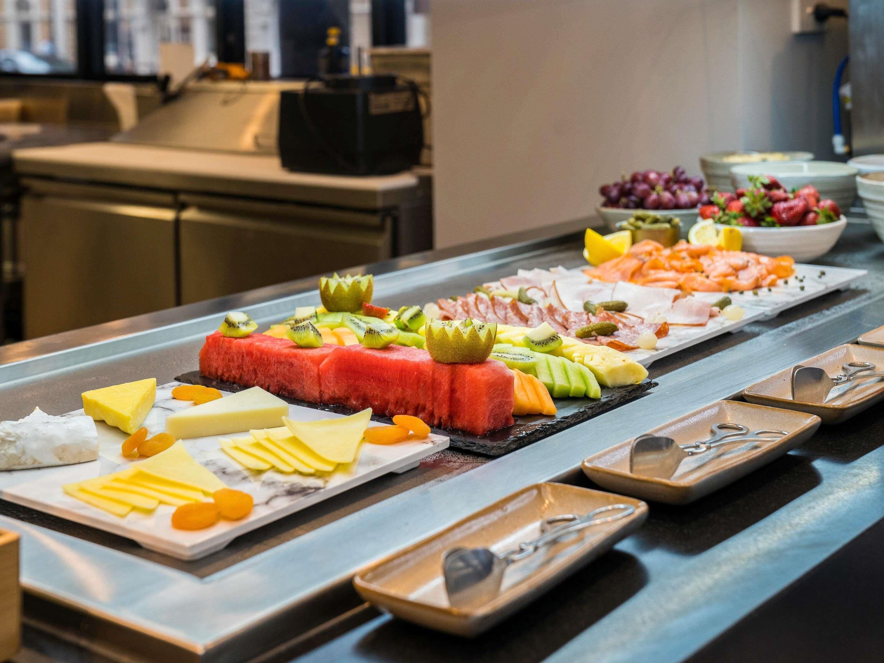 Buffet com diversos alimentos, incluindo frutas, queijos e carnes.