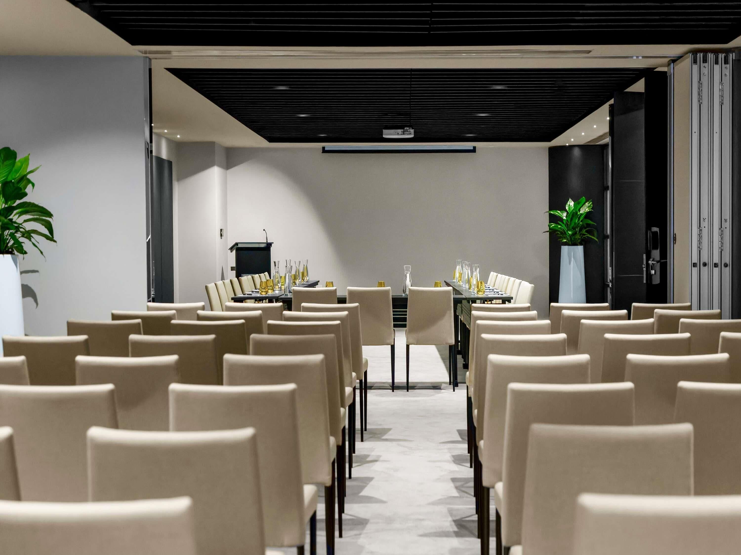 Una sala conferenze con file di sedie, un lungo tavolo e un podio.