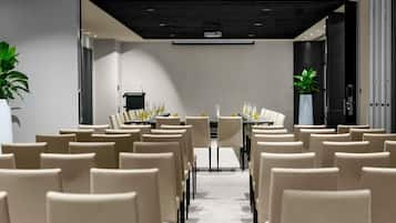 Una sala conferenze con file di sedie, un lungo tavolo e un podio.