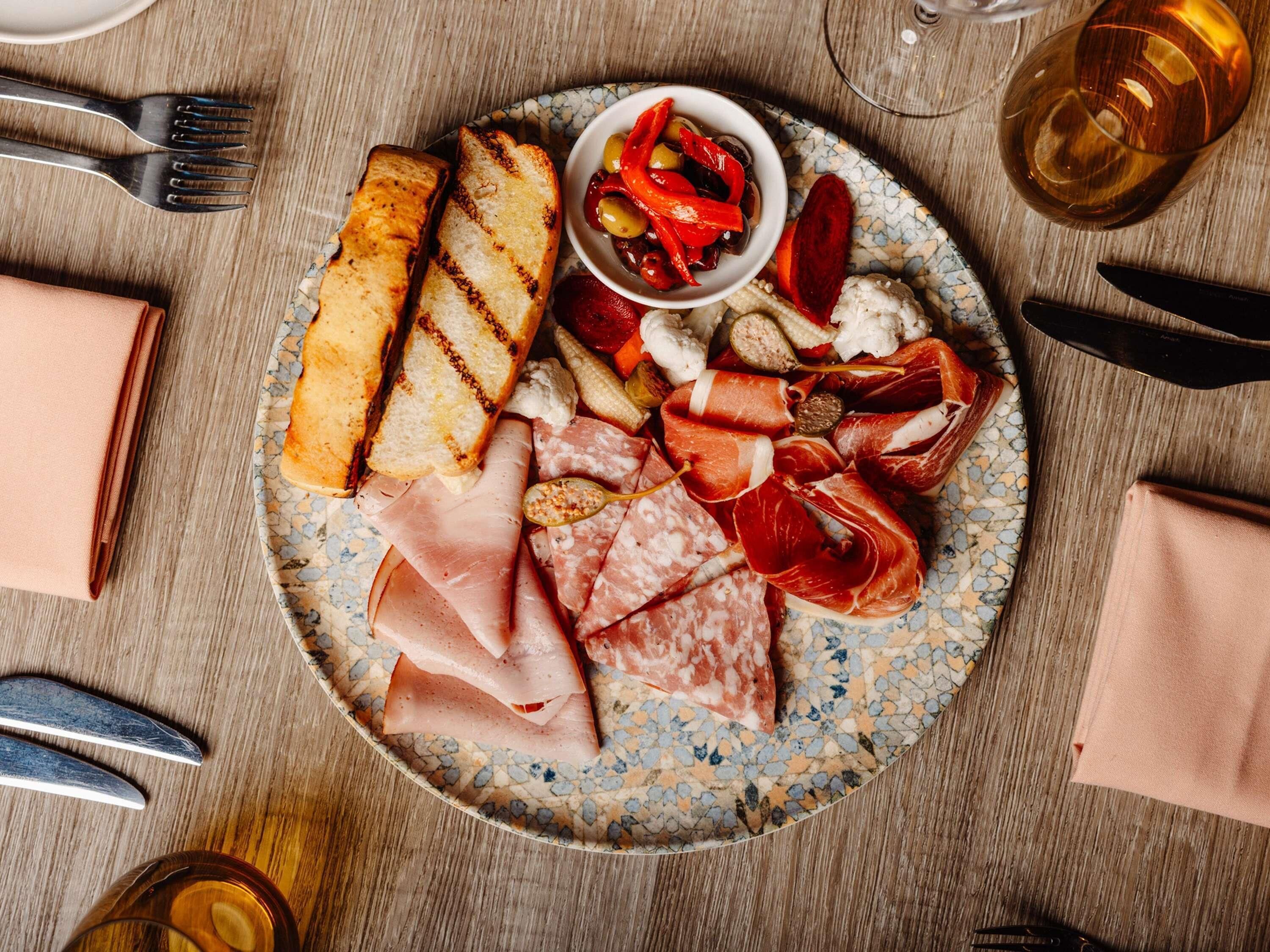A plate of assorted meats, bread, and a small bowl of olives on a table.