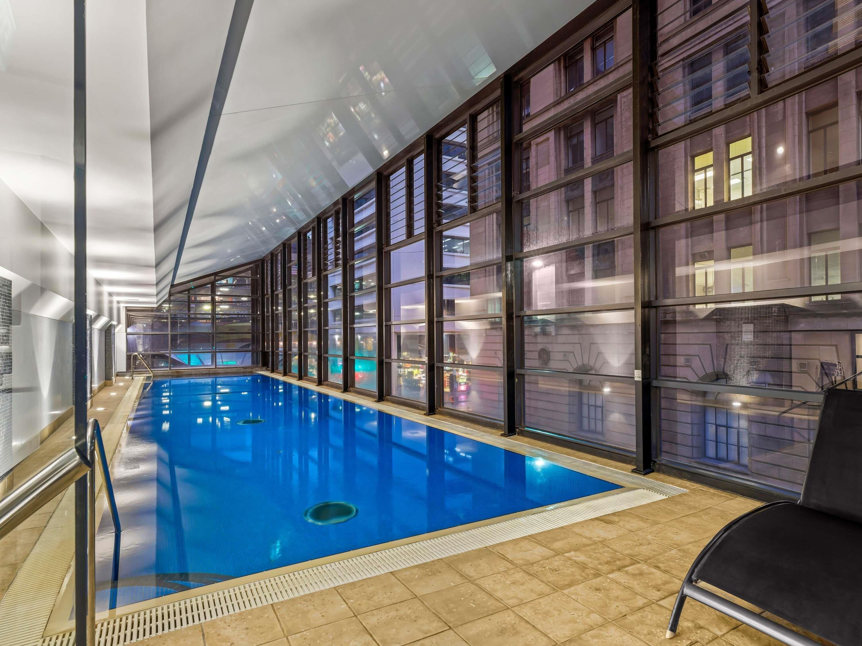 An indoor swimming pool with clear glass walls, a tiled floor, and a black chair near the pool.