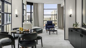 A modern hotel room with a dining area, a seating area with a blue armchair, and a view of the cityscape through large windows. - Peppers Waymouth Adelaide (Adelaide)