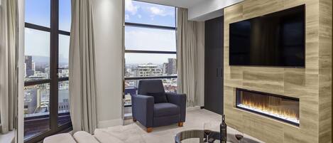 Una sala de estar moderna con sofá, sillón y una mesa de centro de vidrio con vino y aperitivos. También se ve un televisor de pantalla plana y una chimenea.