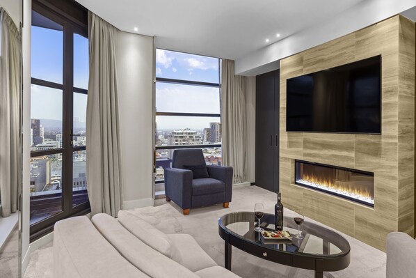 Relax in style with a panoramic city view from the comfort of this living room, featuring a cozy sofa, a dark armchair, and a fireplace.