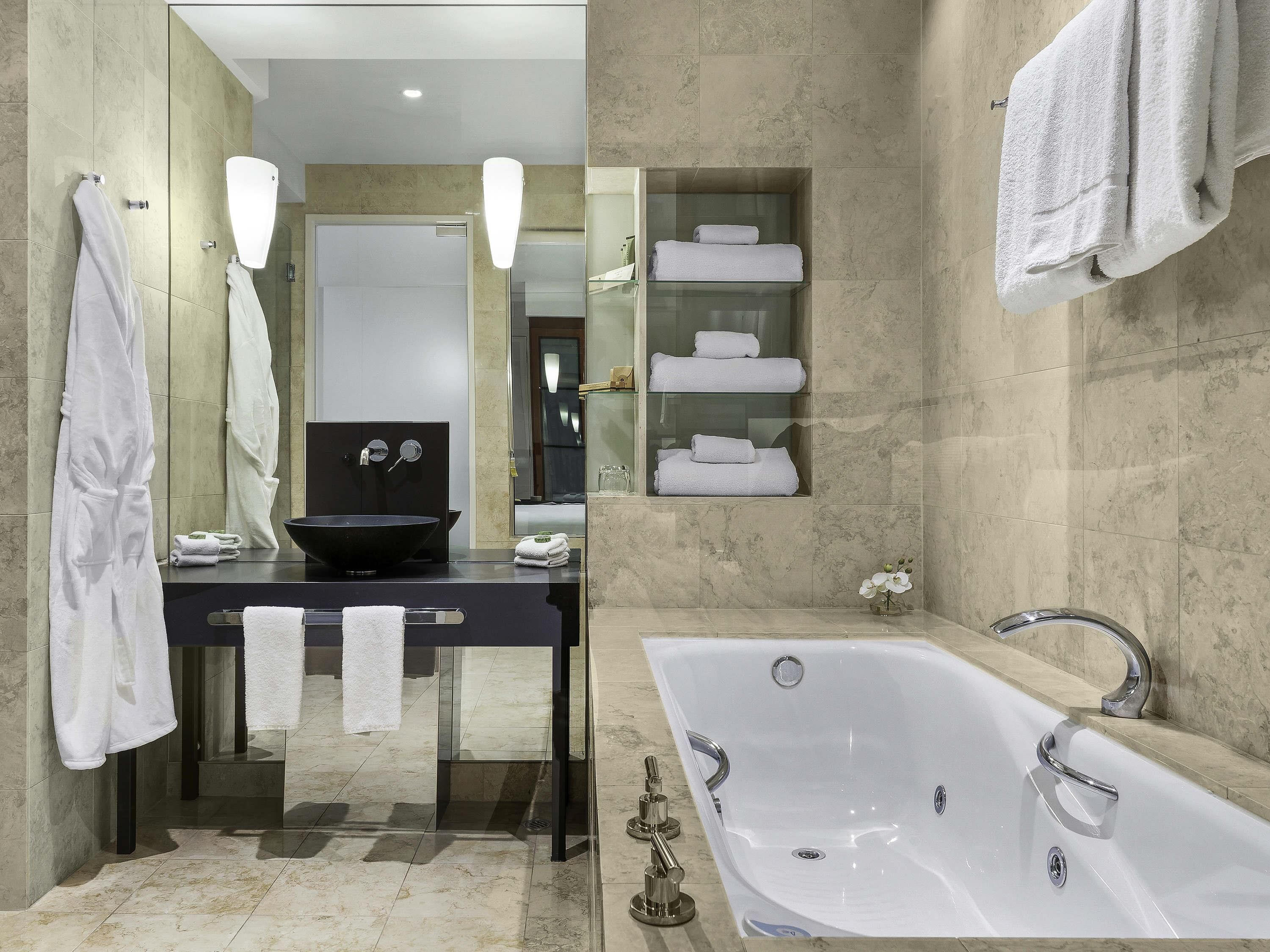 A modern bathroom with a large bathtub, a black sink, and a glass-enclosed vanity.