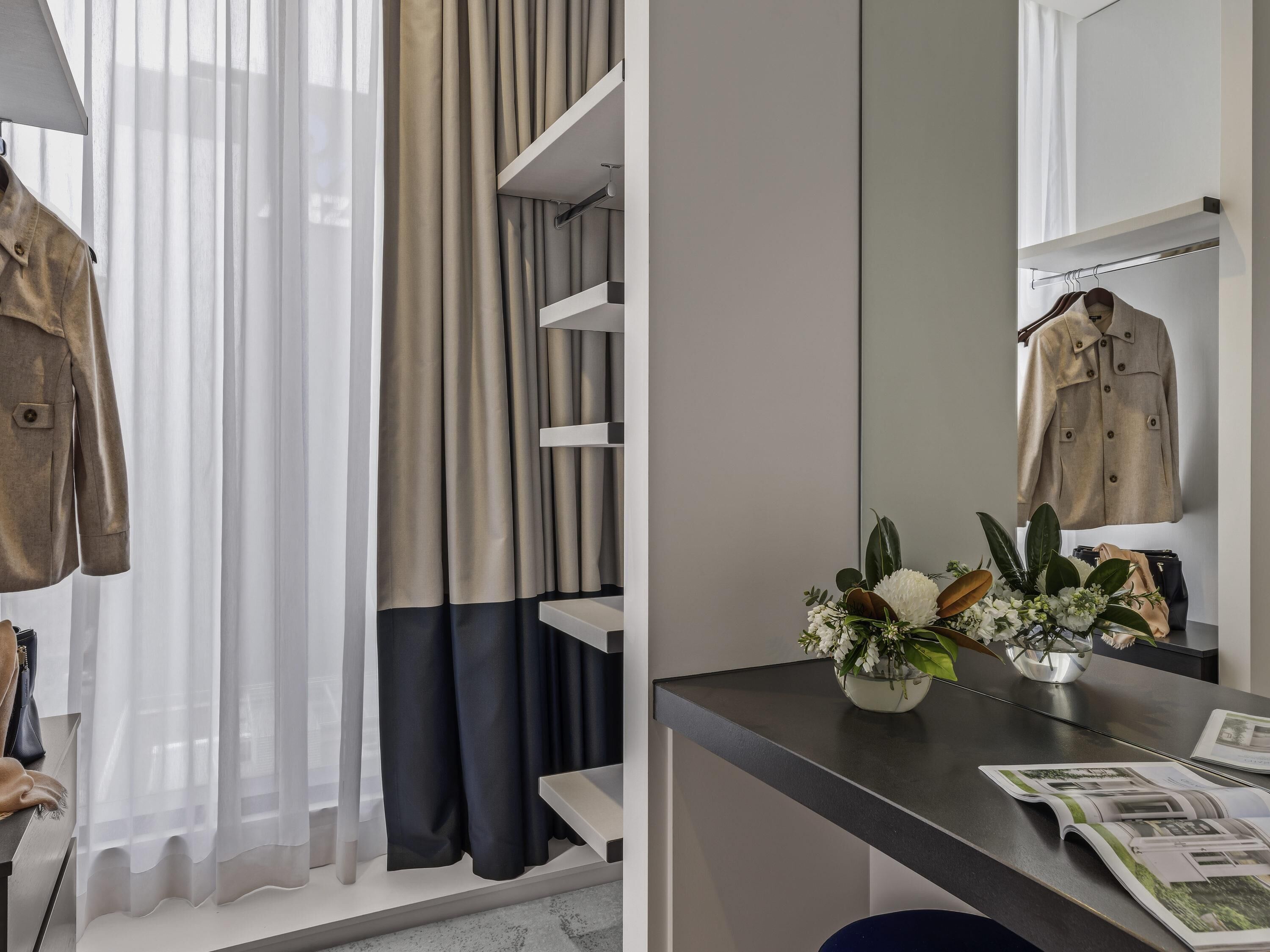 Une chambre moderne dotée d’une armoire intégrée, d’un miroir, d’un bureau agrémenté d’un vase de fleurs et d’un magazine.