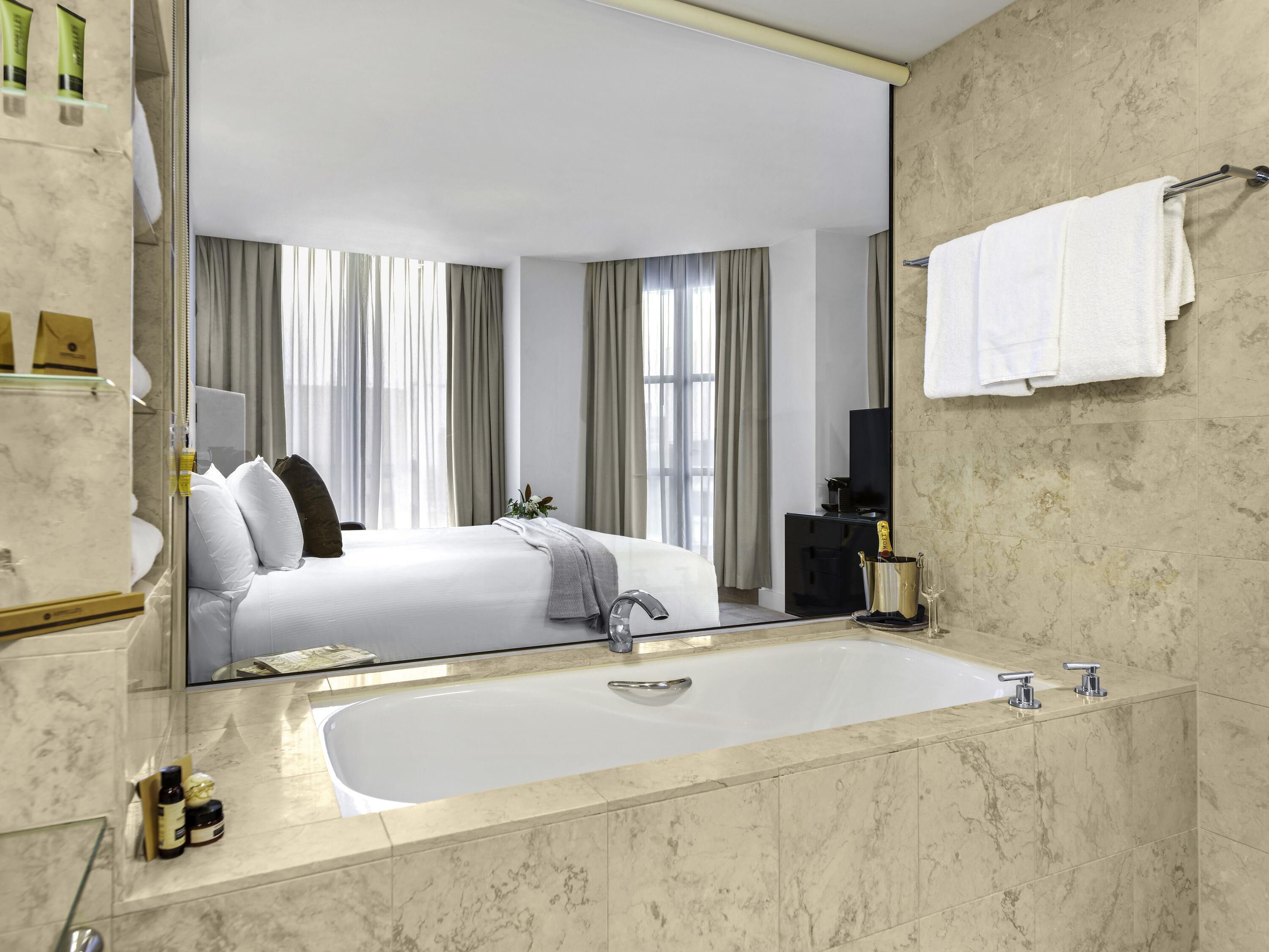 A modern hotel bathroom with a large mirror, a bathtub, and a sink.