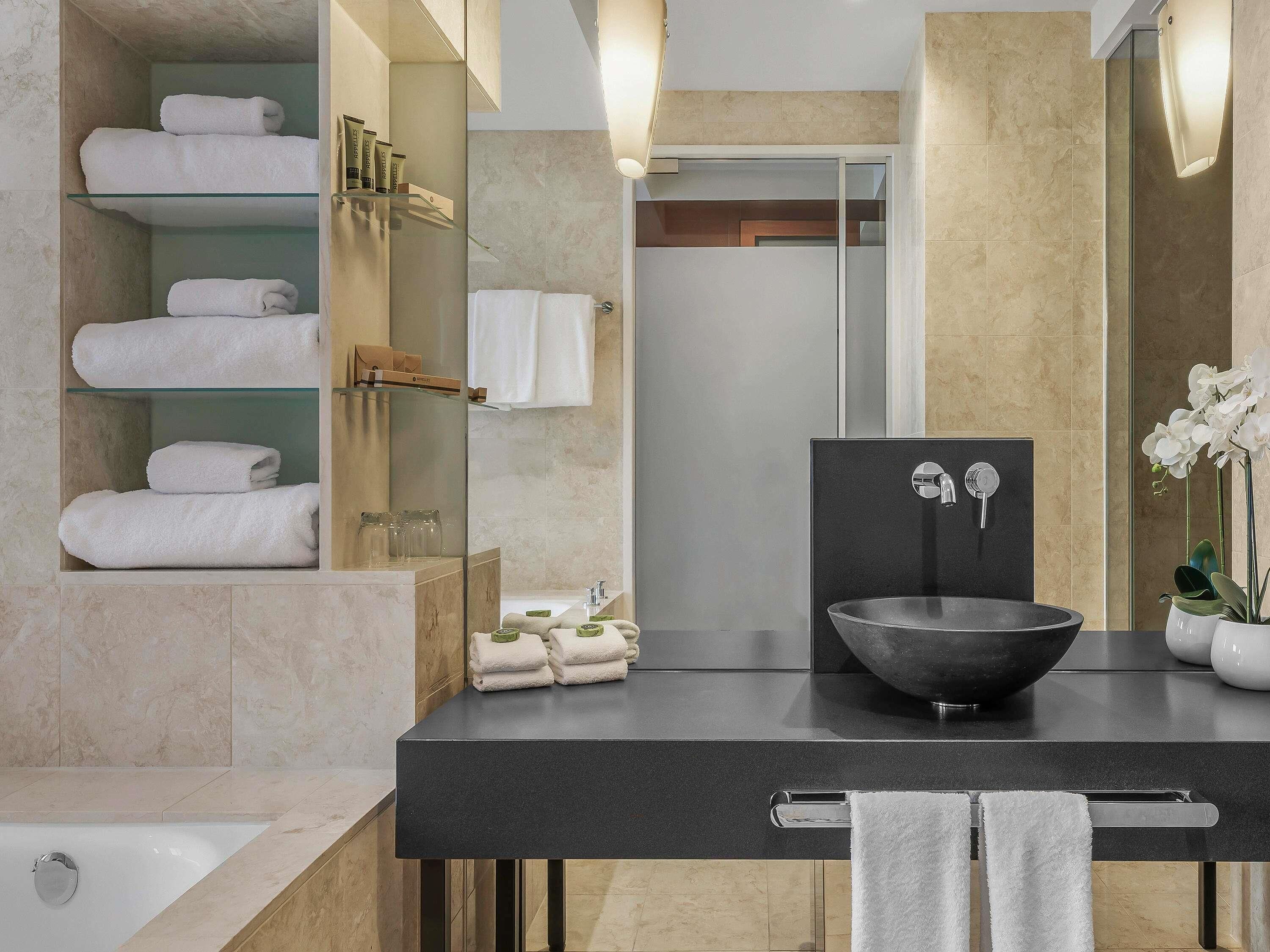 Une salle de bain moderne avec un lavabo noir, une douche en verre et des serviettes soigneusement rangées.