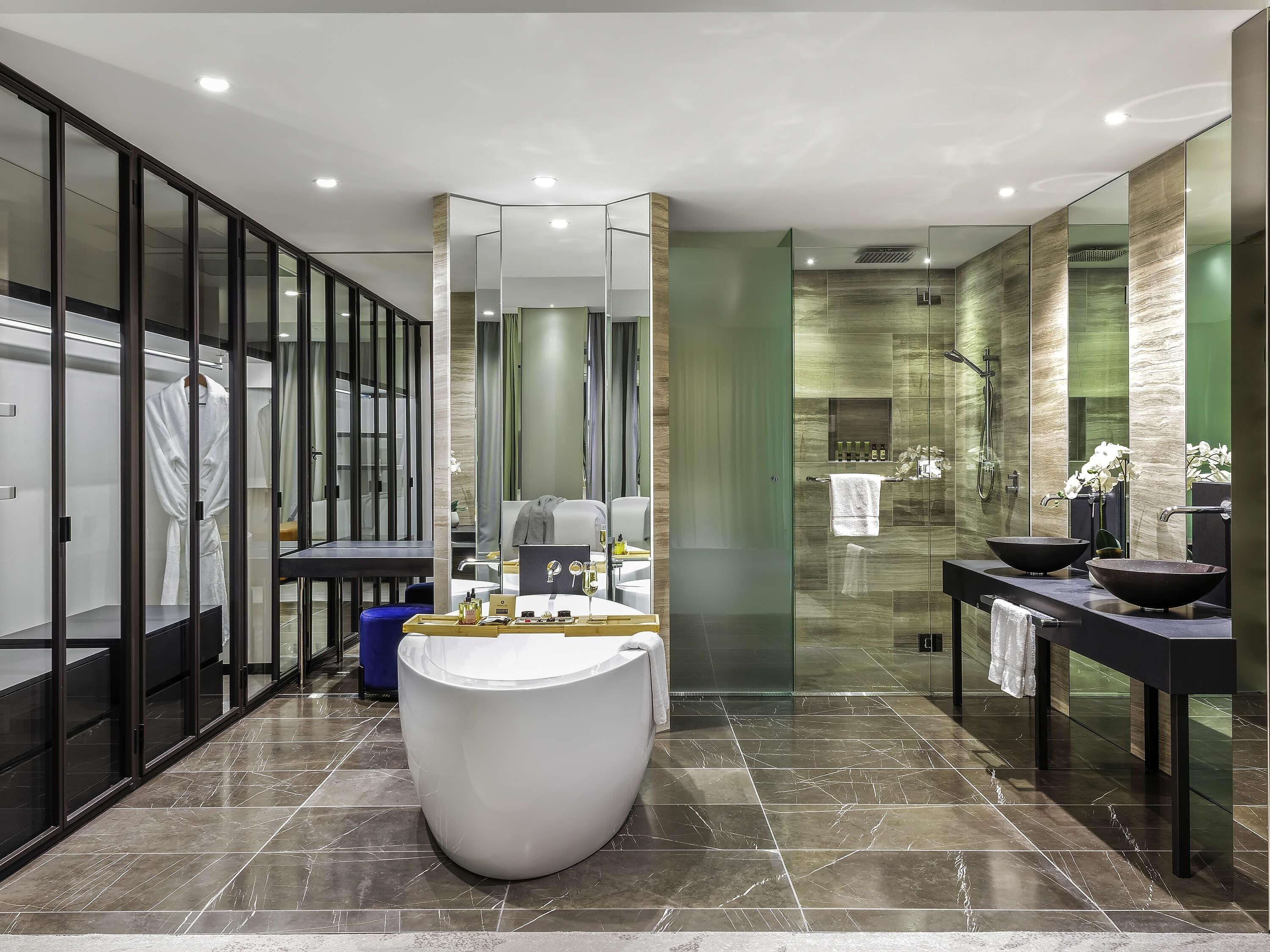 Un baño moderno con una bañera blanca grande, una zona de ducha con mampara de vidrio y un tocador con dos lavamanos.