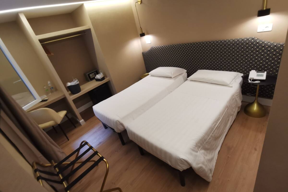 Una camera d'albergo con due letti, una scrivania, una sedia e un armadio.