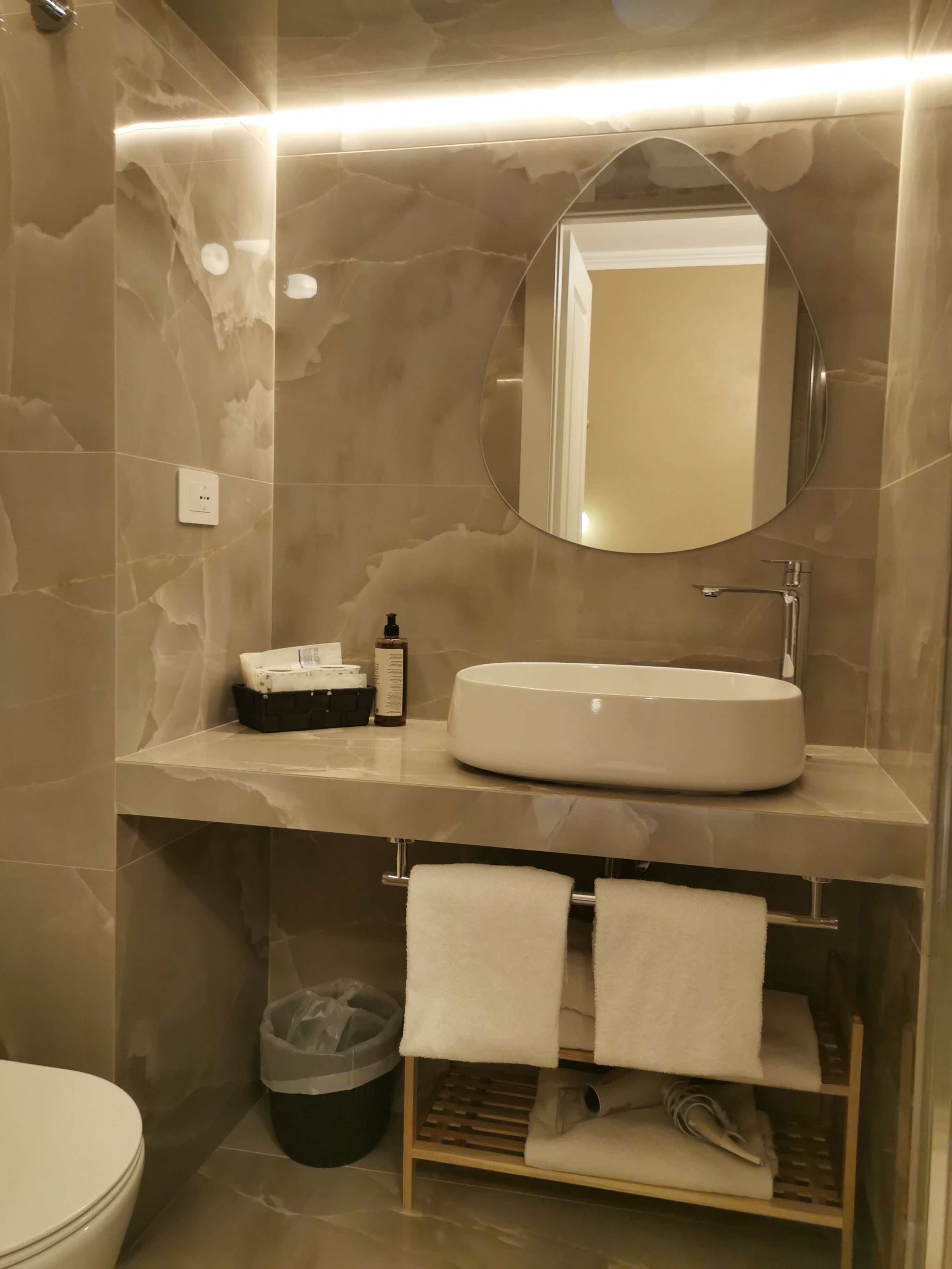 Un baño con pared de mármol, un espejo redondo, un lavamanos y un perchero para toallas.