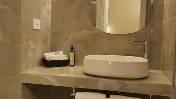 Un baño con pared de mármol, un espejo redondo, un lavamanos y un perchero para toallas.