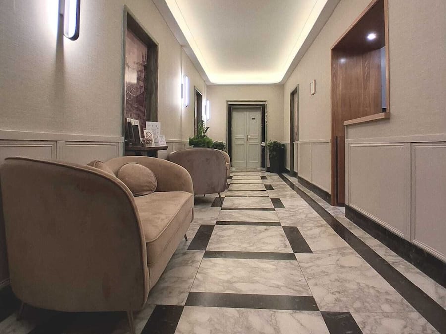 Un couloir d’hôtel avec un sol à carreaux, un canapé et une porte au fond.