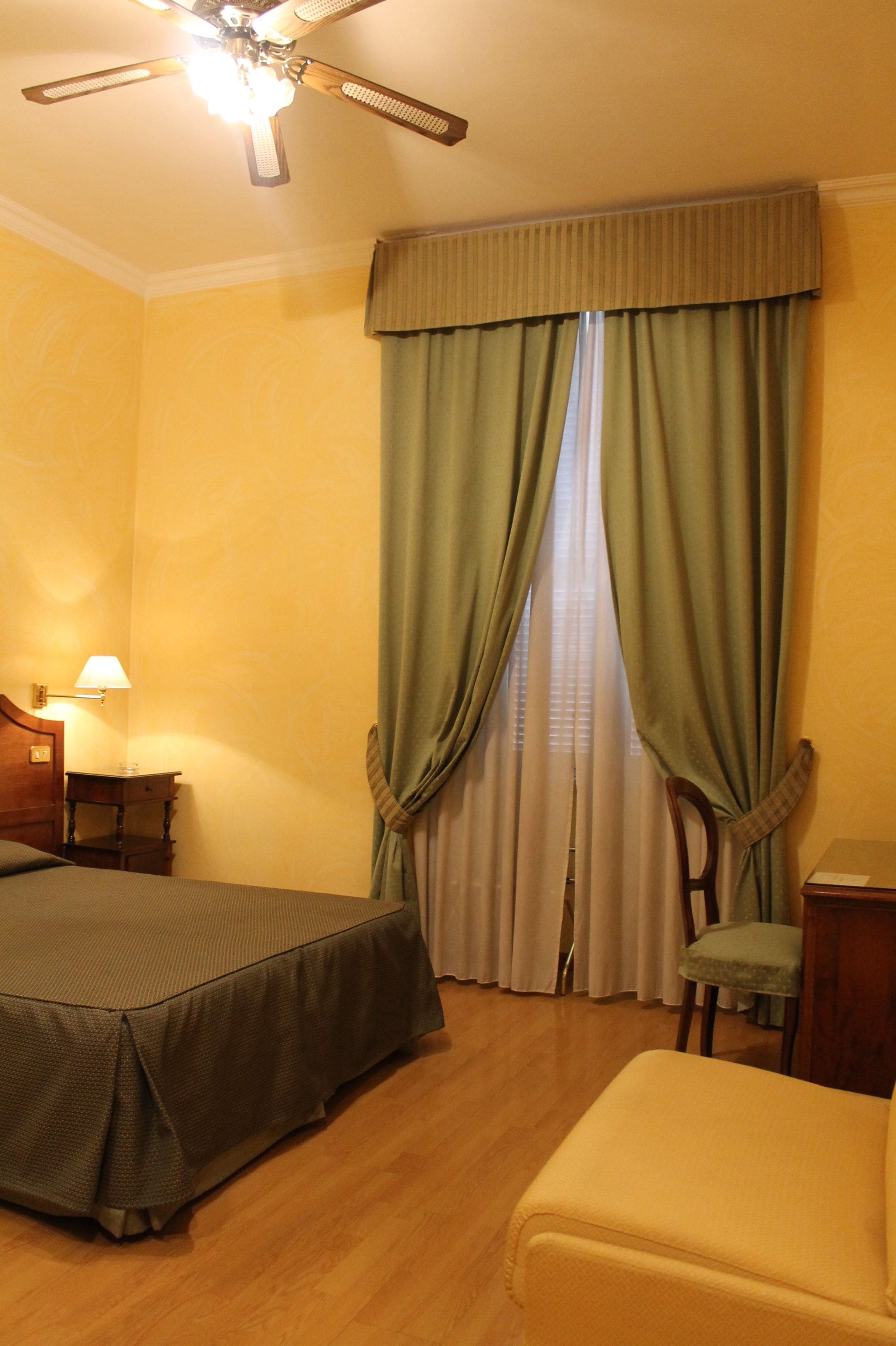 Ein Hotelzimmer mit einem Bett, einem Sessel, einem Schreibtisch und einem Deckenventilator.