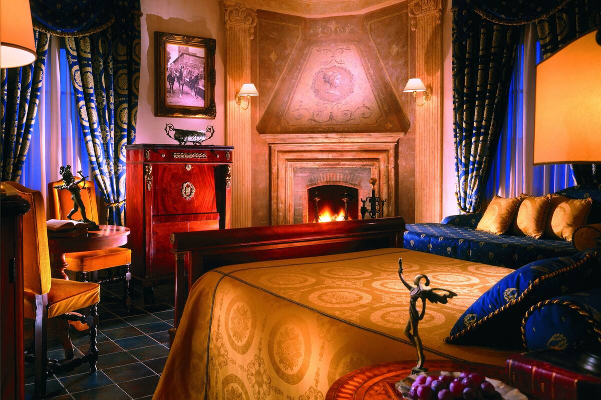 A room with a fireplace, a bed with blue and gold bedding, a wooden desk, and a chair.