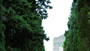 A couple walking down a tree-lined path towards a stone building with a tower. - Castello della Castelluccia (Rome)