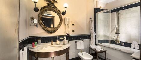 A bathroom with a marble sink, a bidet, a toilet, and a large mirror with wall sconces.