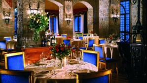 A restaurant with multiple tables set for dining, featuring blue upholstered chairs and ornate chandeliers. - Castello della Castelluccia (Rome)