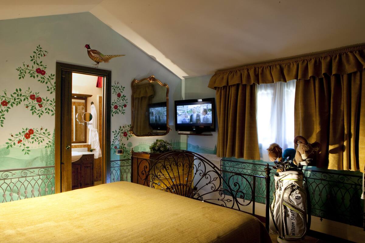 A bedroom with a bed, a television, a mirror, and a window with curtains.