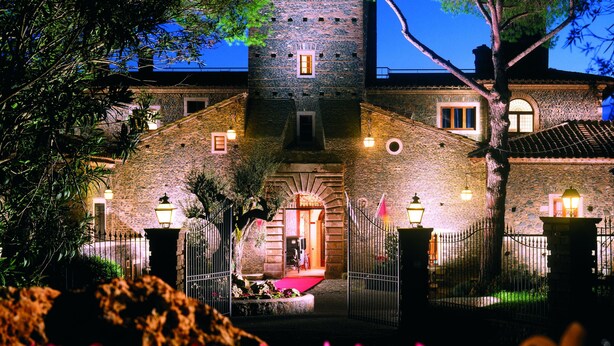 A stone building with a tower, a red carpet, and a metal fence. - Castello della Castelluccia (Rome)