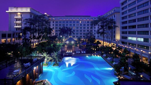 A hotel with a large swimming pool surrounded by palm trees and lounge chairs. - Dong Fang Hotel Guangzhou (Guangzhou)