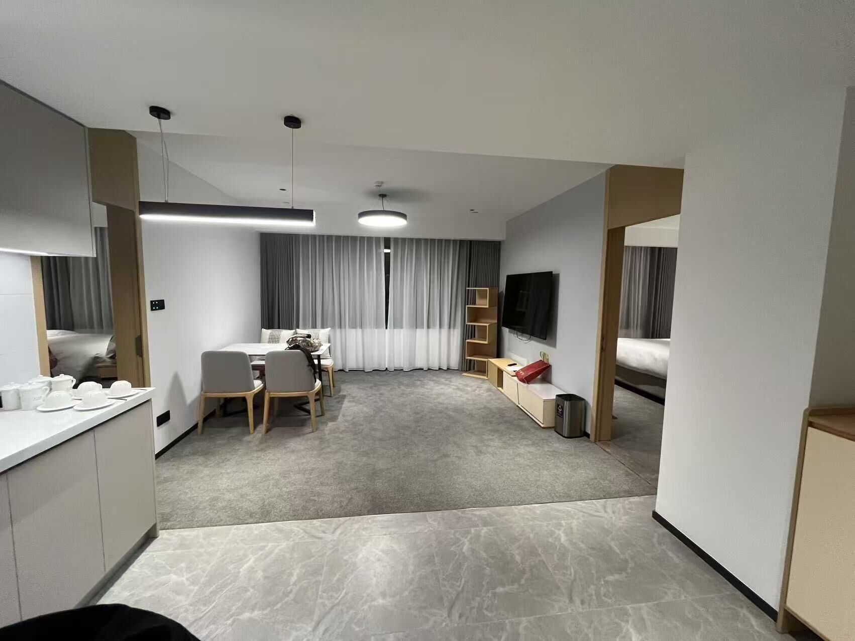 A modern hotel room with a dining area, a TV, a bed, and a small kitchenette.