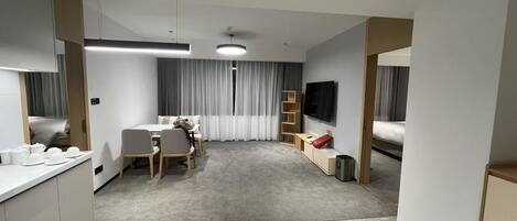 A modern hotel room with a dining area, a TV, a bed, and a small kitchenette.