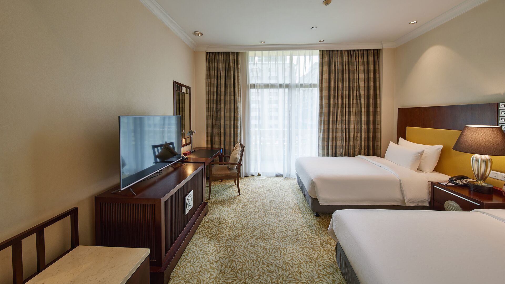 A hotel room with a TV, two beds, a desk, and a chair.