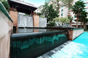 A pool with a waterfall feature, lounge chairs, and a building with a tiled roof in the background. - Dong Fang Hotel Guangzhou (Guangzhou)