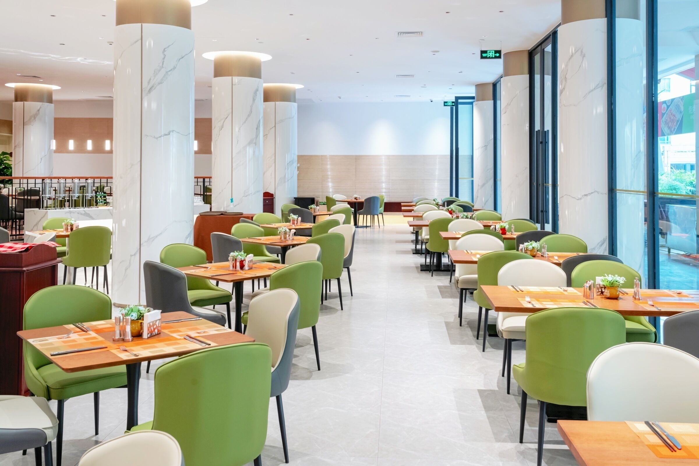 A spacious dining area with green and white chairs, marble pillars, and a long counter.