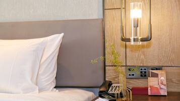 A hotel room with a bed, a bedside table with a phone, a vase with a plant, and a wall-mounted light fixture.