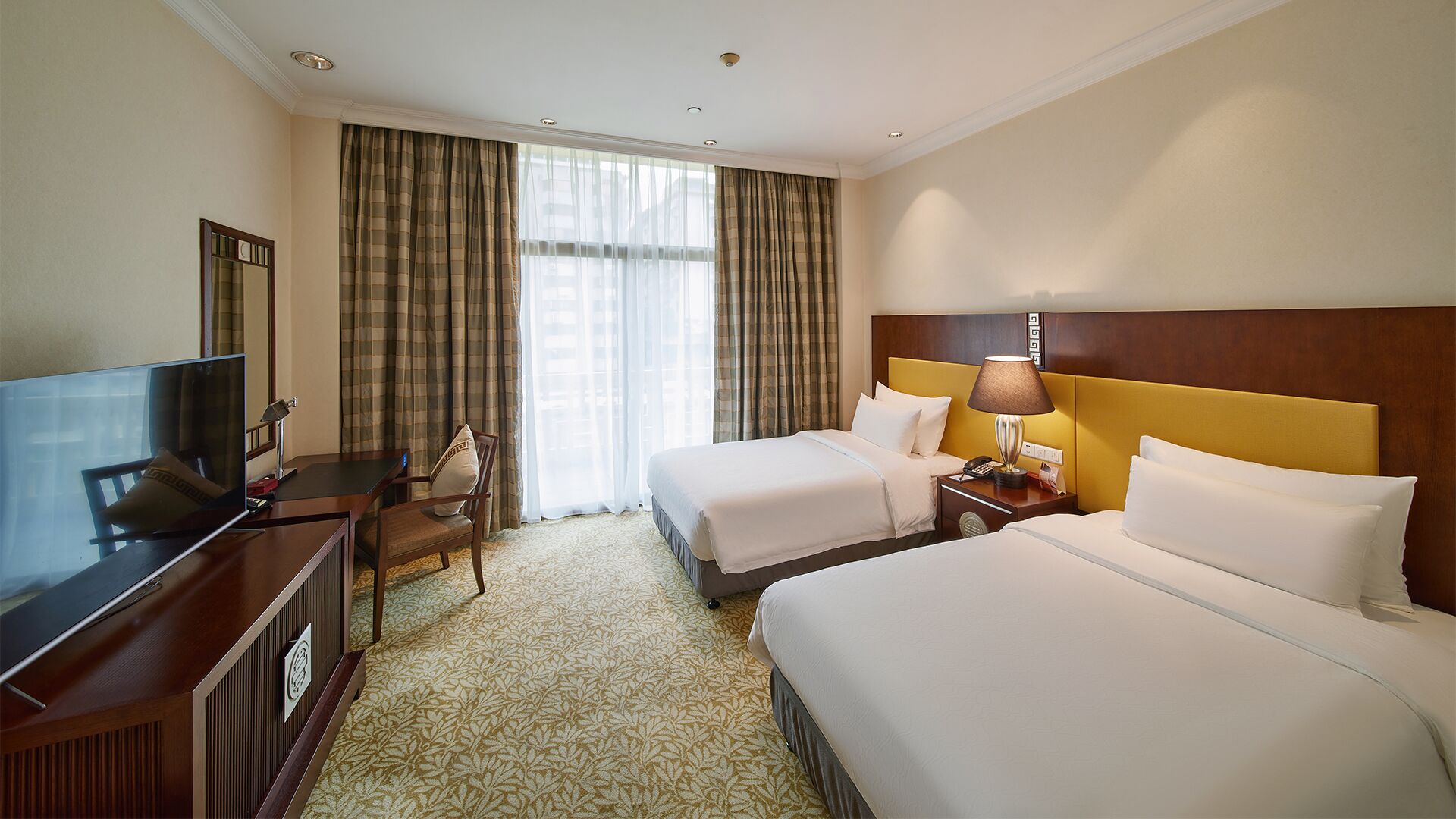 A hotel room with two beds, a desk with a television, a chair, and a nightstand with a lamp.