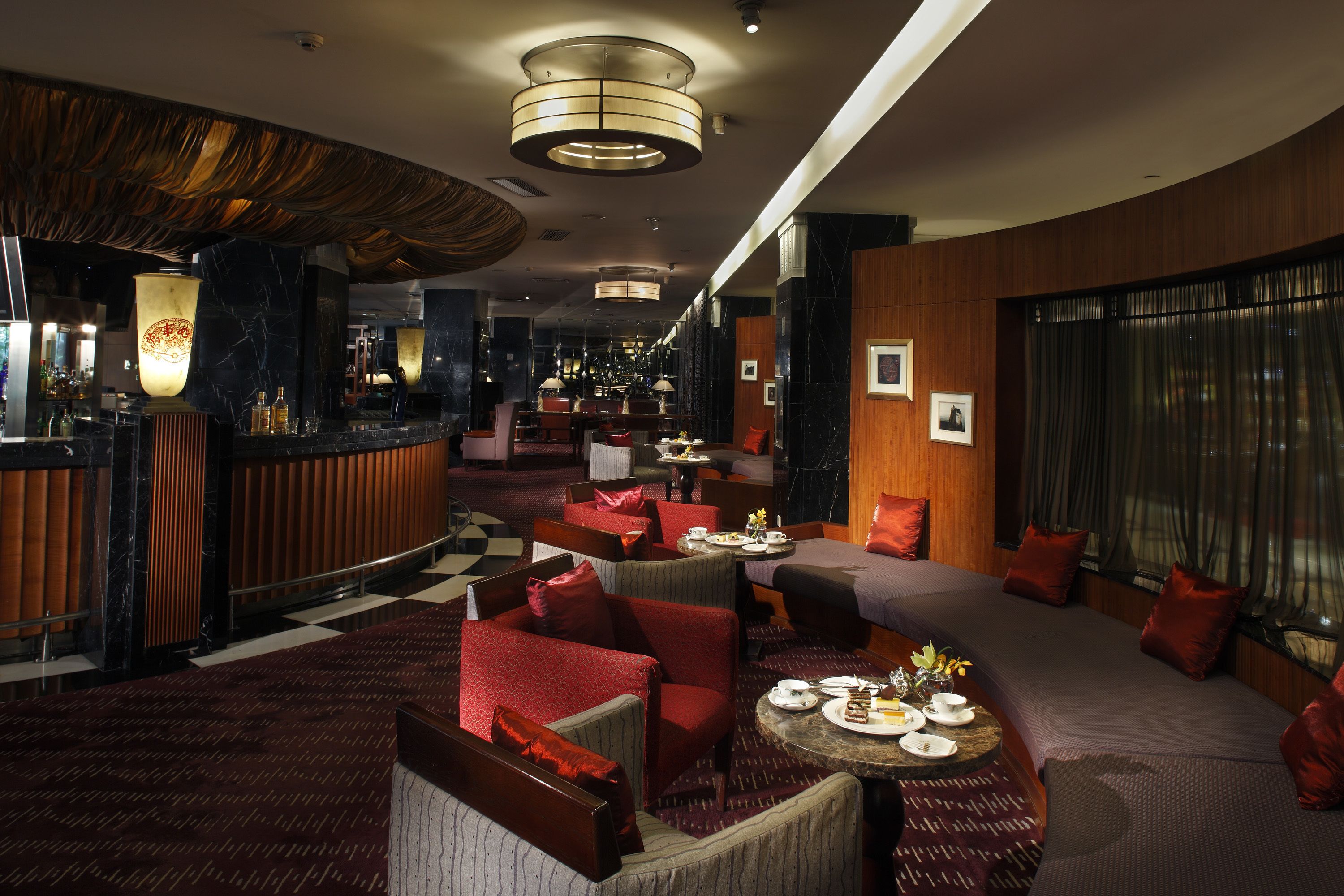A modern hotel lobby with a checkered floor, red upholstered seating, and a bar area with a marble countertop.