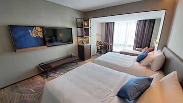 A hotel room with two beds, a TV, a desk, and a balcony with curtains.