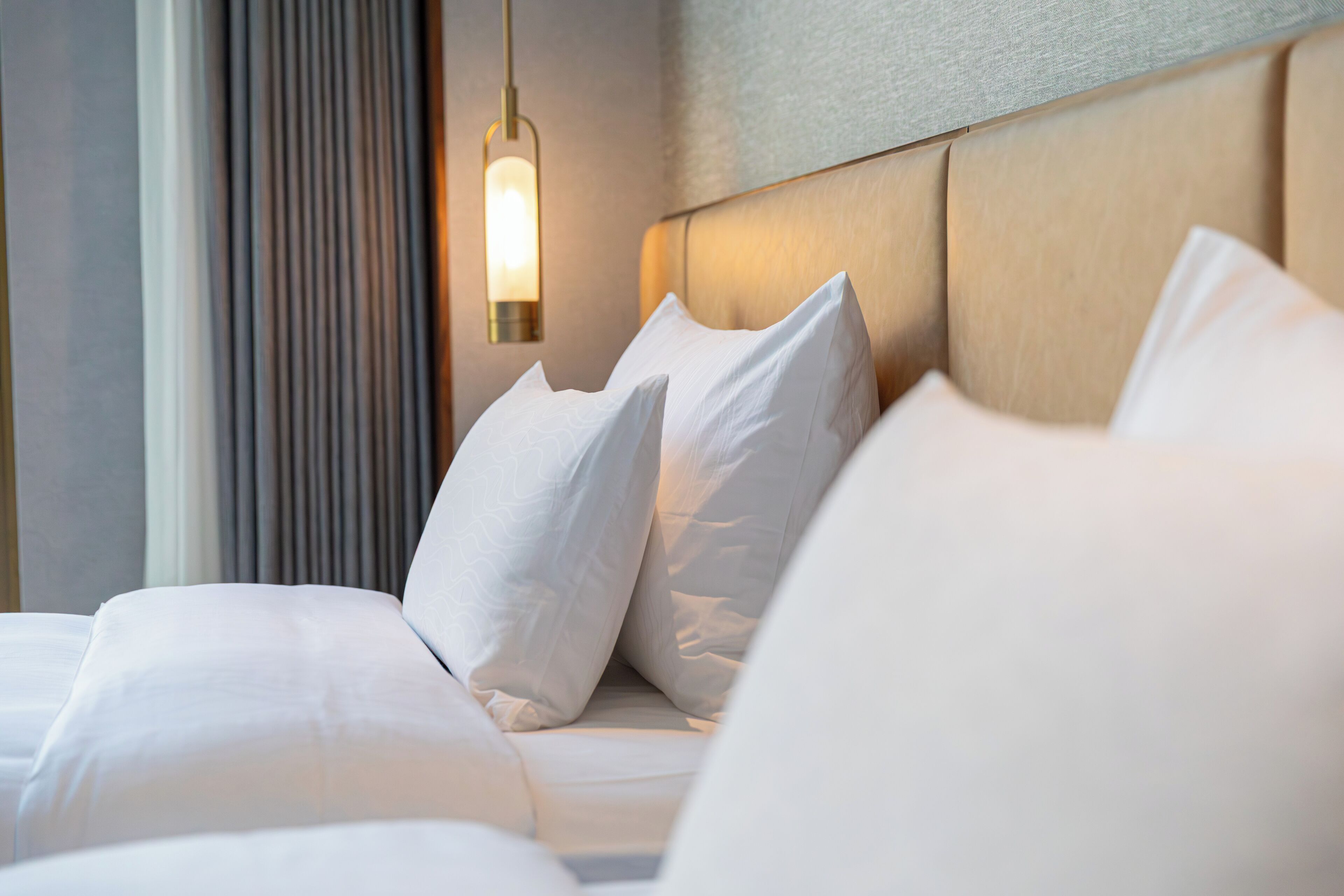Un lit bien fait, avec du linge de lit blanc et des oreillers, une tête de lit au fini texturé et un luminaire fixé au mur.