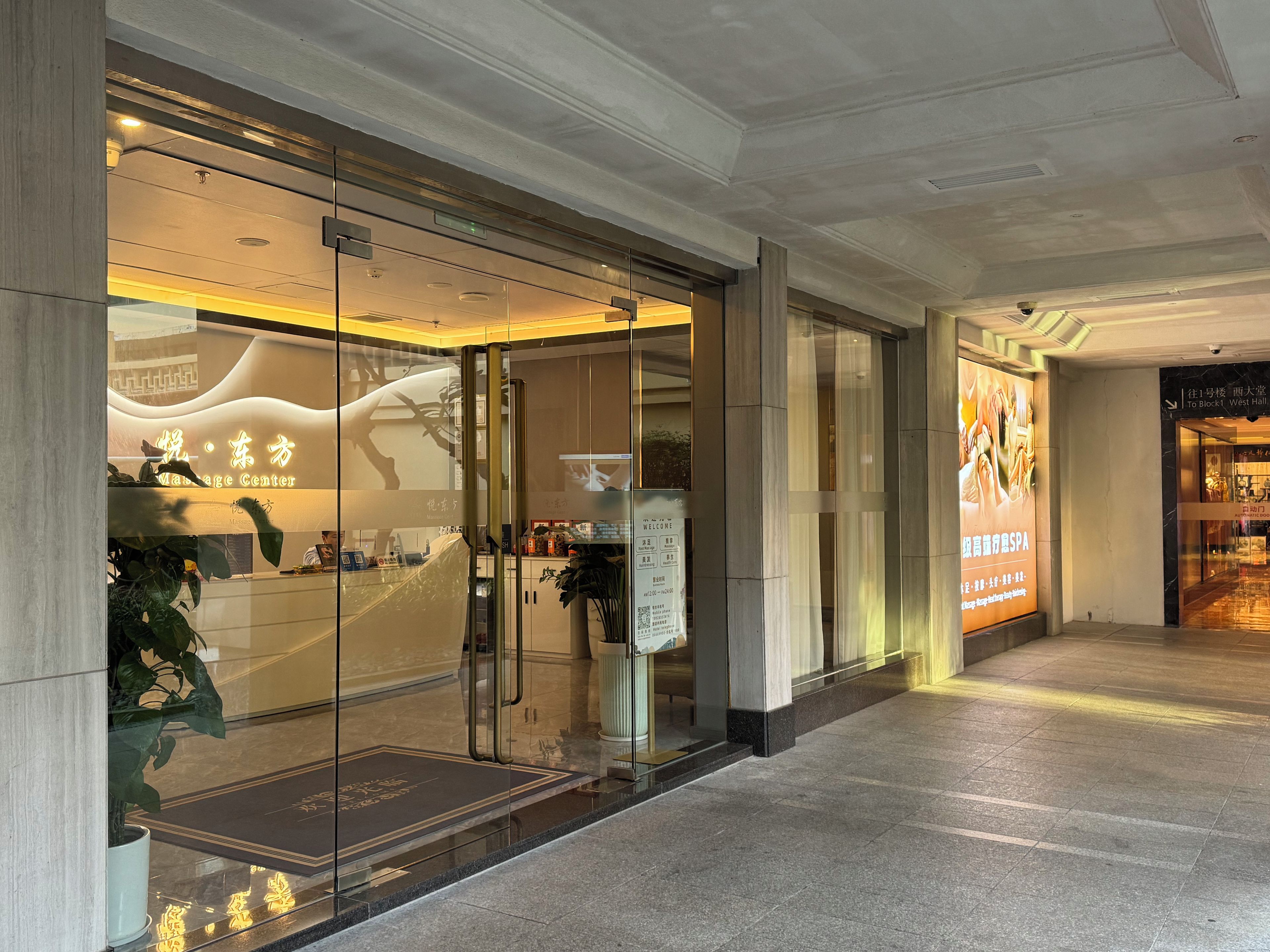 Entrada de un edificio moderno con puertas de cristal, una zona de recepción y un cartel que indica un spa.