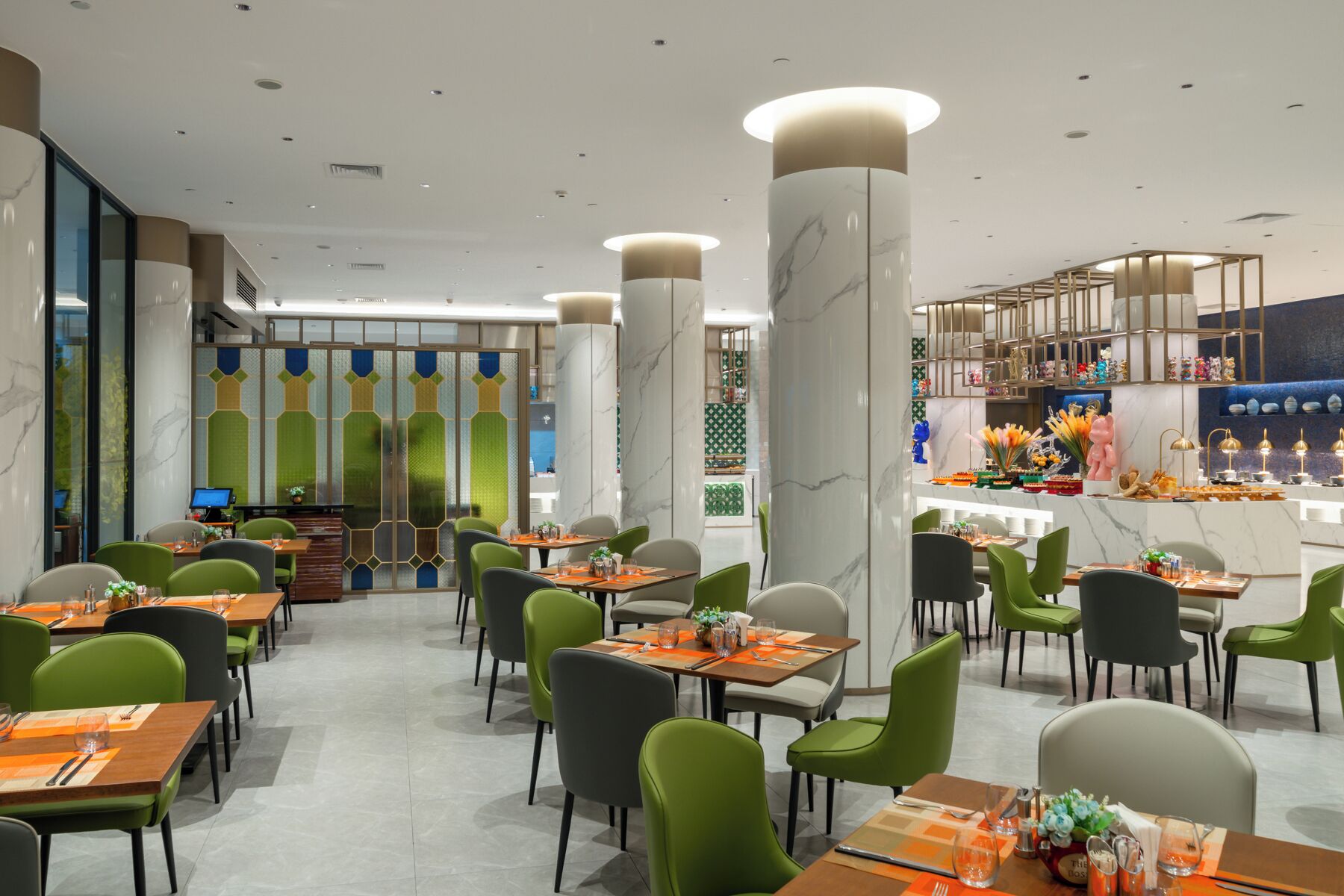 Un restaurante moderno con sillas verdes, columnas de mármol y una zona de bar central.