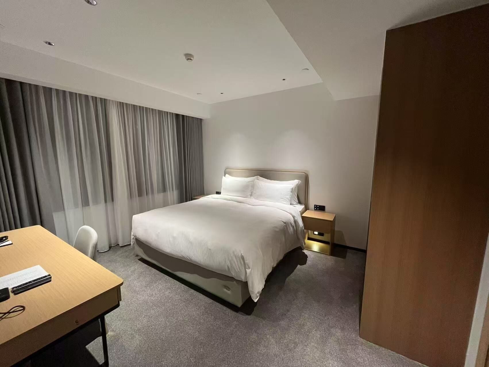 A hotel room with a bed, bedside table, and a desk with a chair.