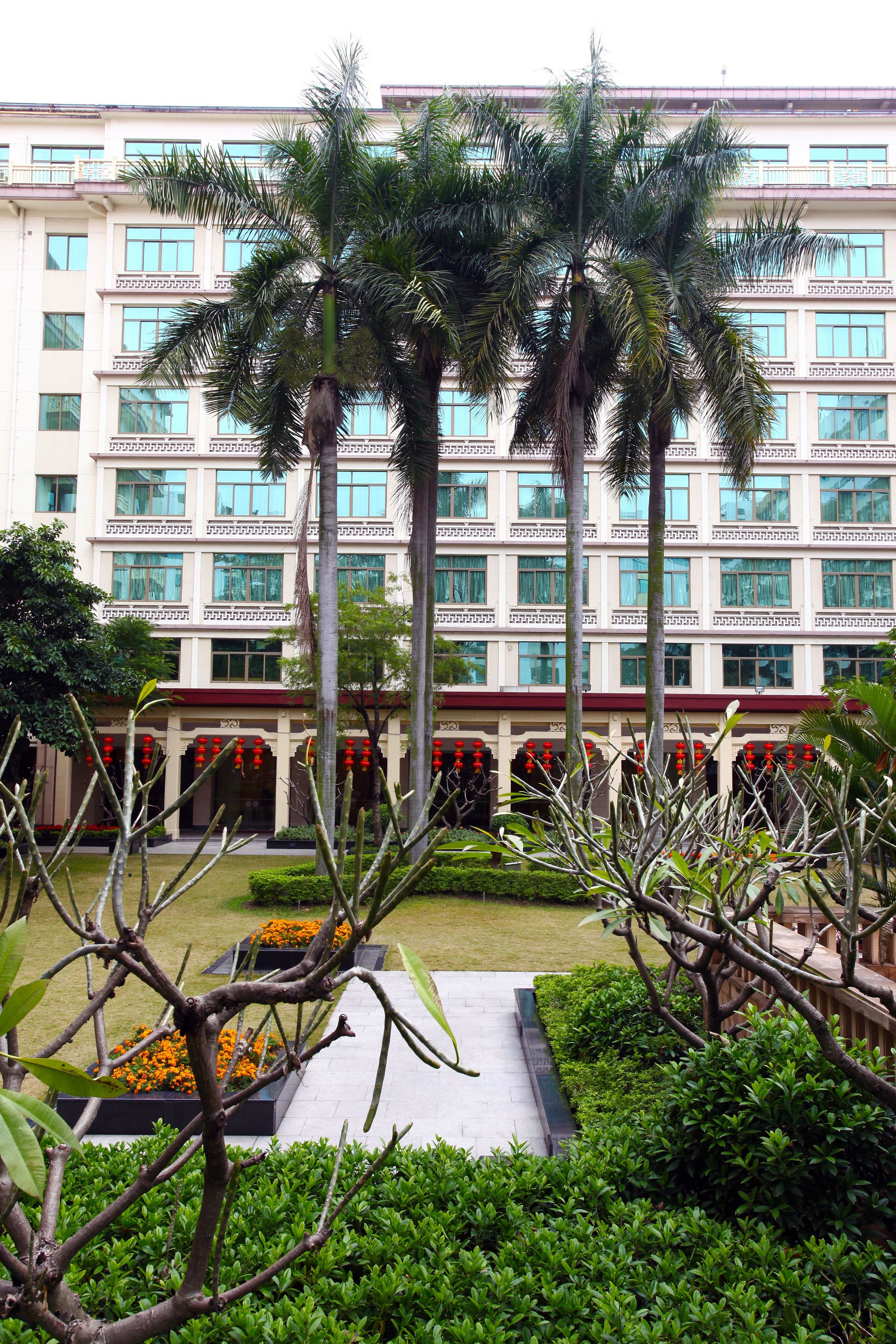 A hotel with a modern facade, multiple floors, and a well-maintained garden with palm trees and flower beds.