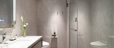A modern bathroom with a large mirror, two sinks, a toilet, and a glass-enclosed shower.