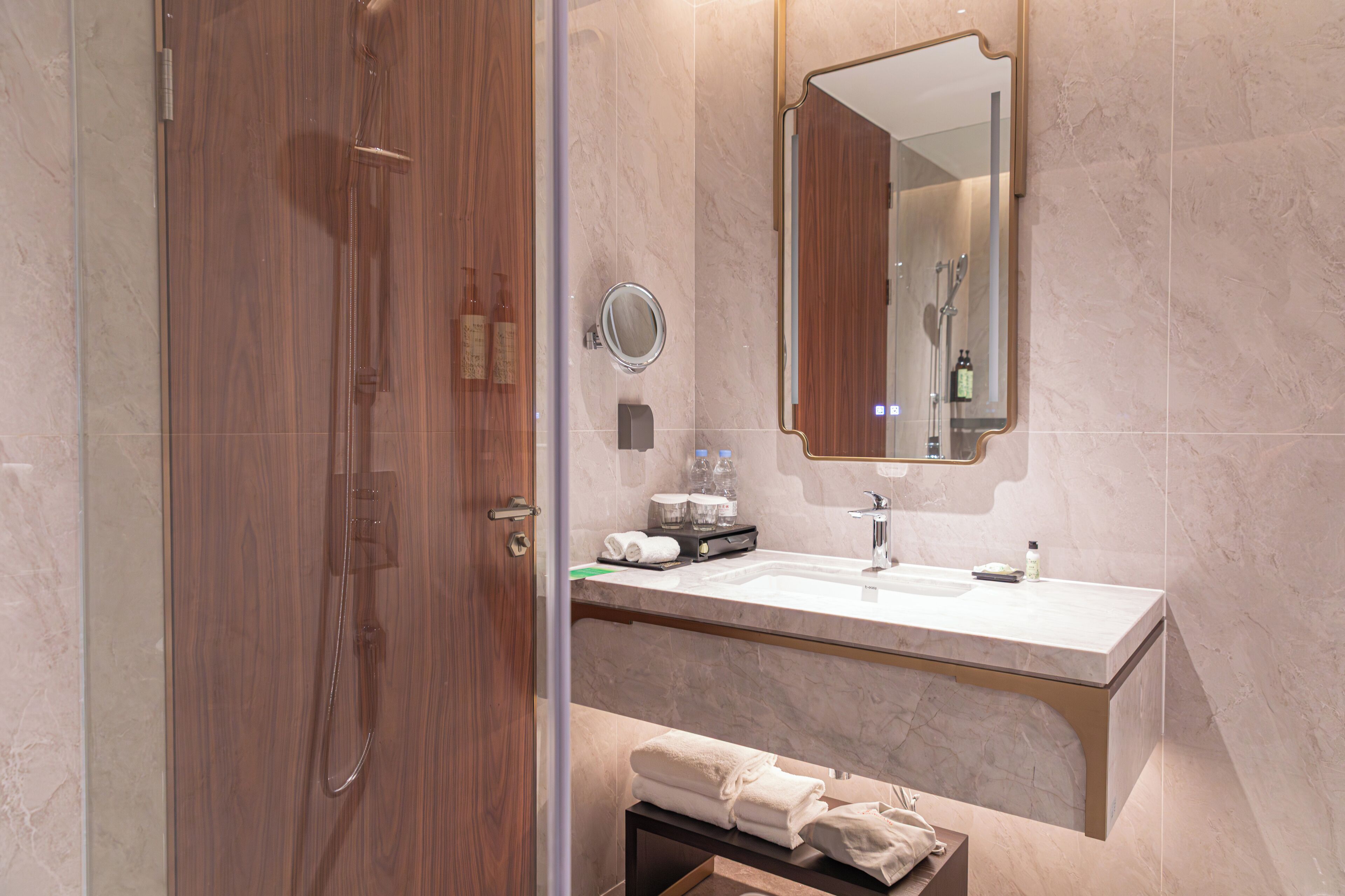 A modern bathroom with a wooden door, a glass shower enclosure, a marble sink, and a large mirror.