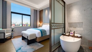 A modern hotel room with a large bed, a sitting area with a chair and a small table, a large bathtub, and a city view through the window. - Dong Fang Hotel Guangzhou (Guangzhou)