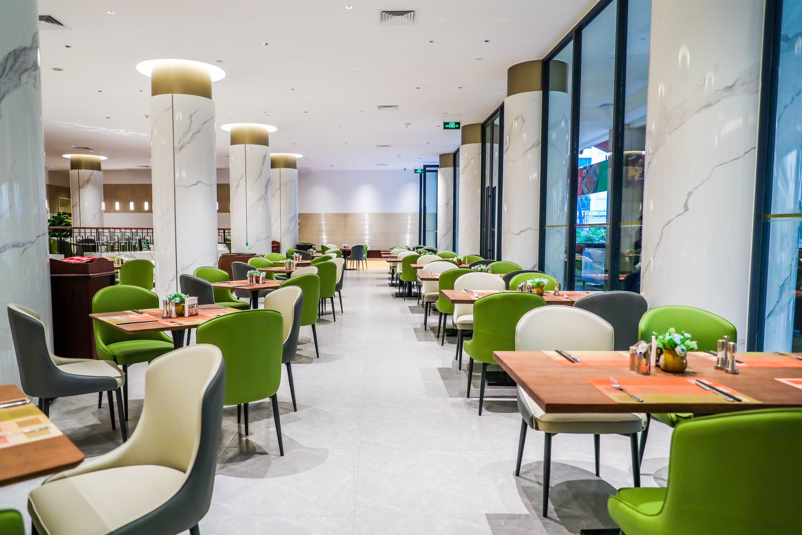 Uma sala de jantar moderna com cadeiras verdes e bege, colunas de mármore e uma mesa longa.