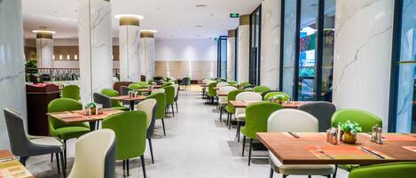 A modern dining area with green and beige chairs, marble columns, and a long table layout.